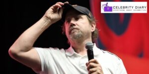 Jamie Kennedy holding a microphone in one hand and adjusting his cap with the other, 2025.